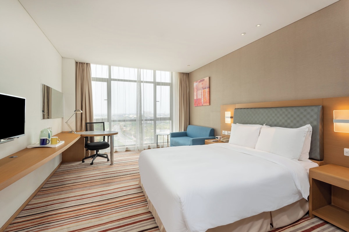A hotel room with a large bed, a desk with a chair, a television, and a window with curtains.