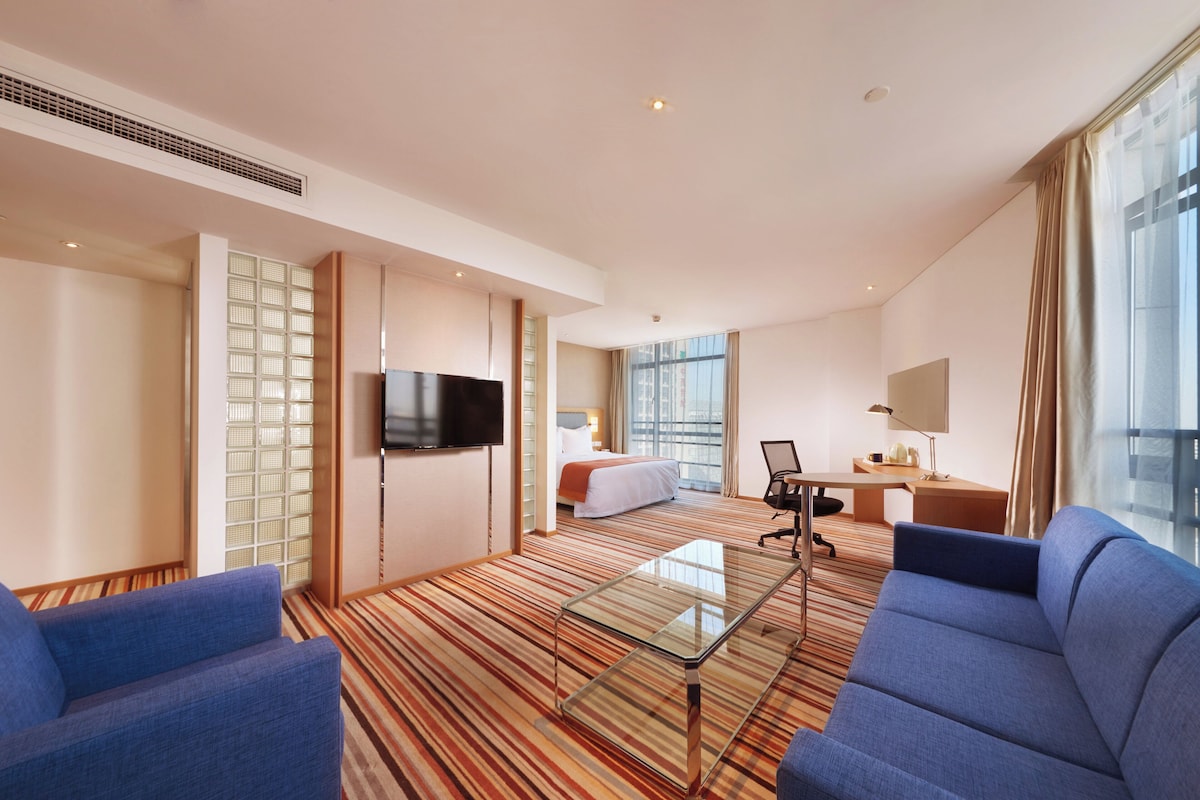 A hotel room with a bed, a desk, a television, and a seating area with a glass coffee table.