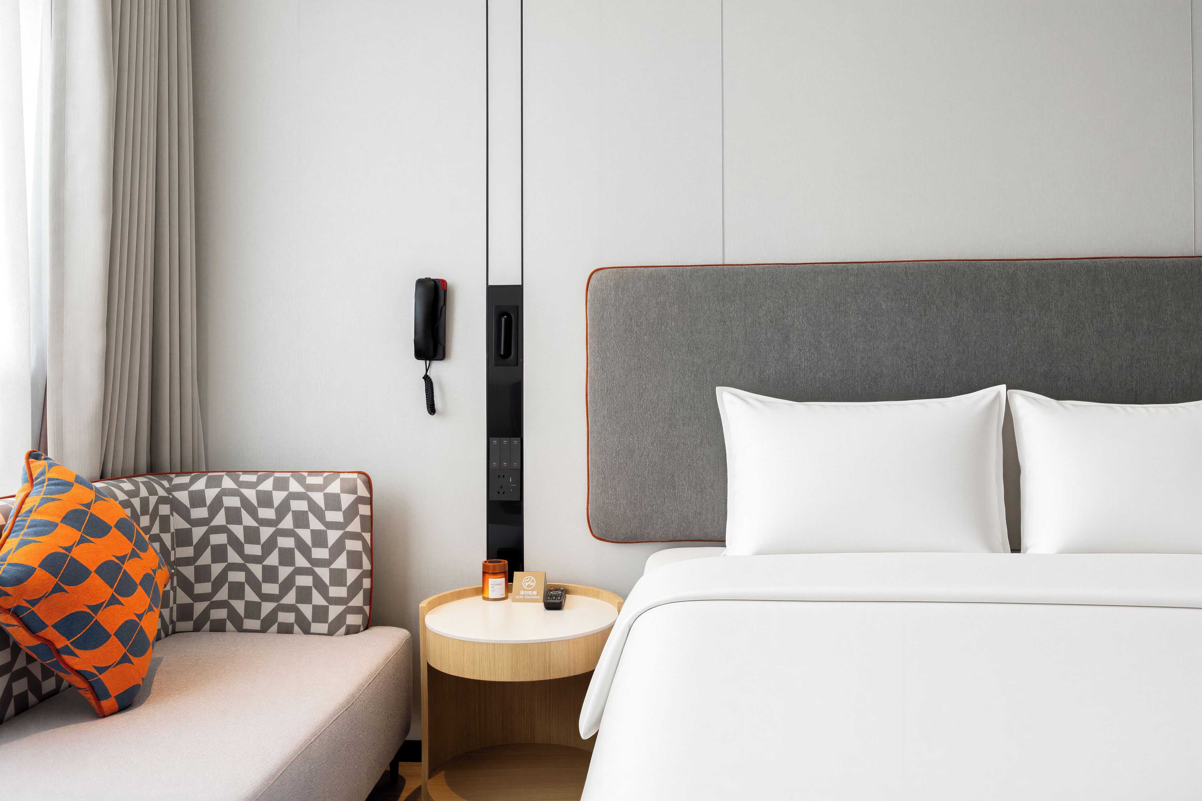 A hotel room with a bed, a bedside table, a chair, and a wall-mounted phone.