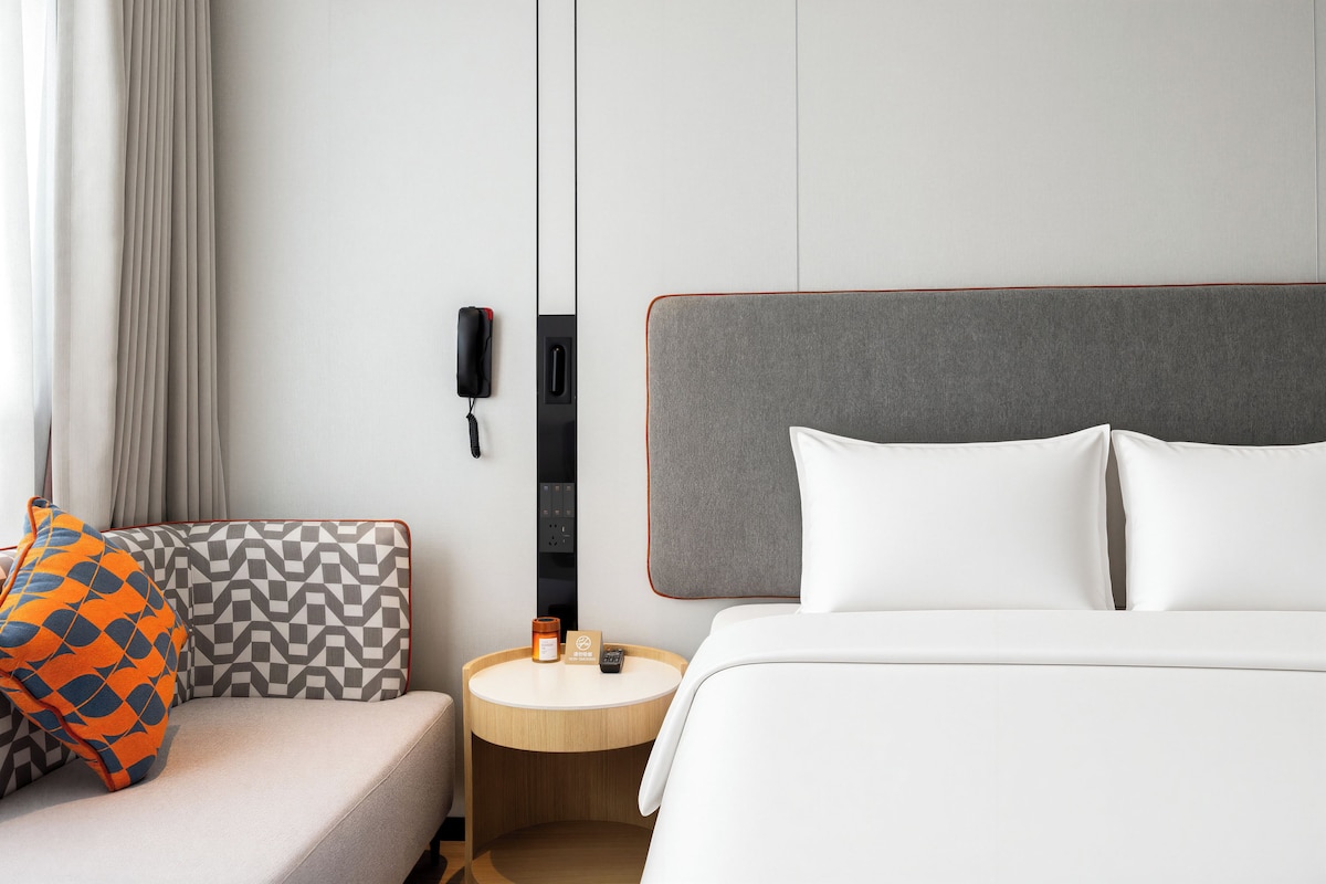A hotel room with a bed, a bedside table, a chair, and a wall-mounted phone.