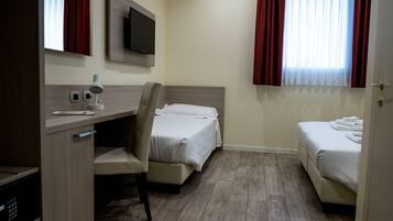 A hotel room with a desk, chair, two beds, a TV, and a window with curtains.