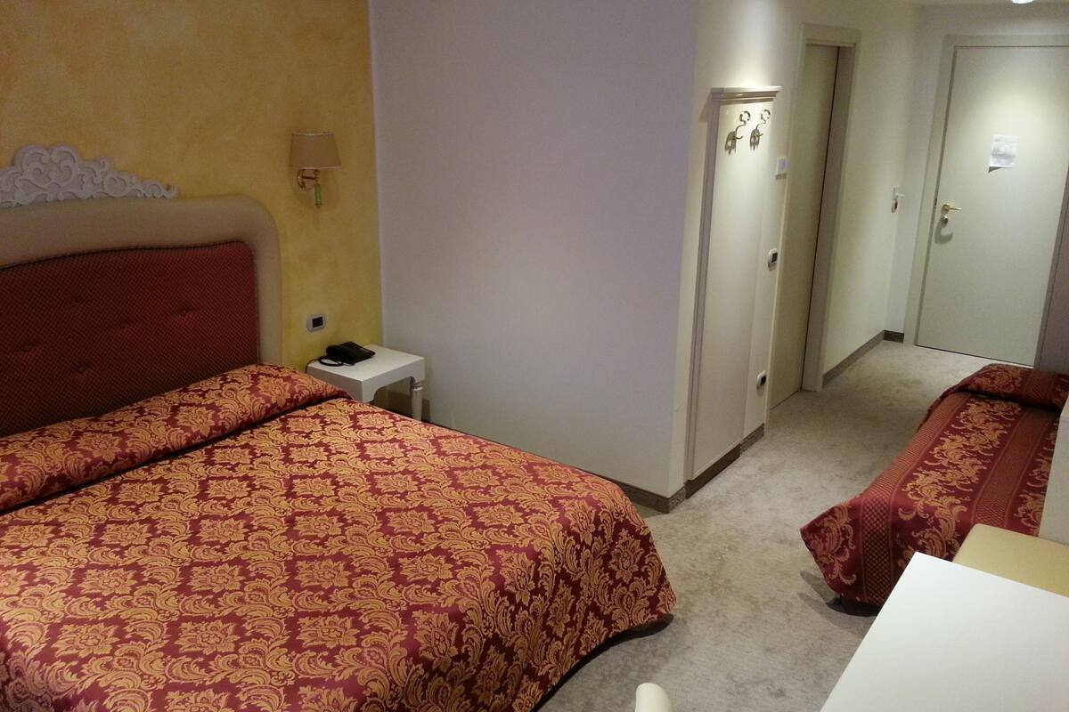 Een hotelkamer met twee bedden, een klein nachtkastje met een lamp, en een deur naar een andere kamer.