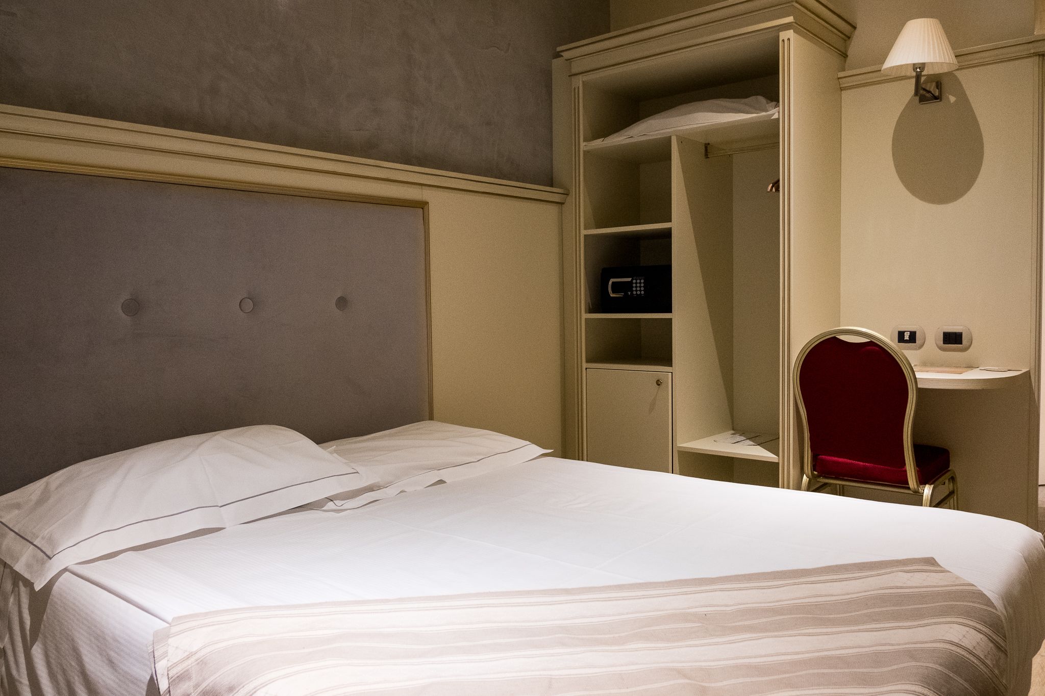 A hotel room with a bed, a wardrobe, and a vanity with a mirror.