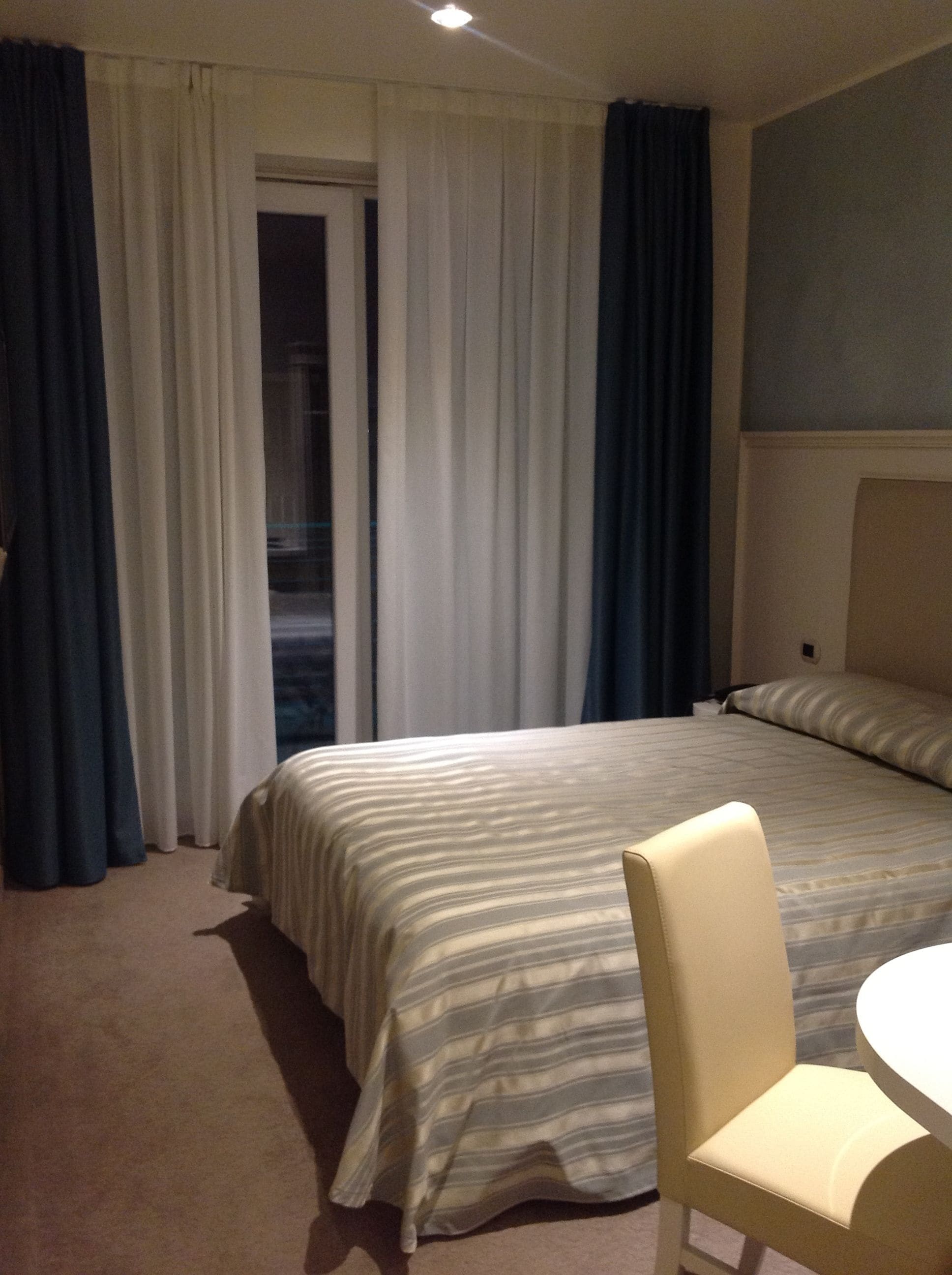 A hotel room with a bed, a chair, a table, and curtains.