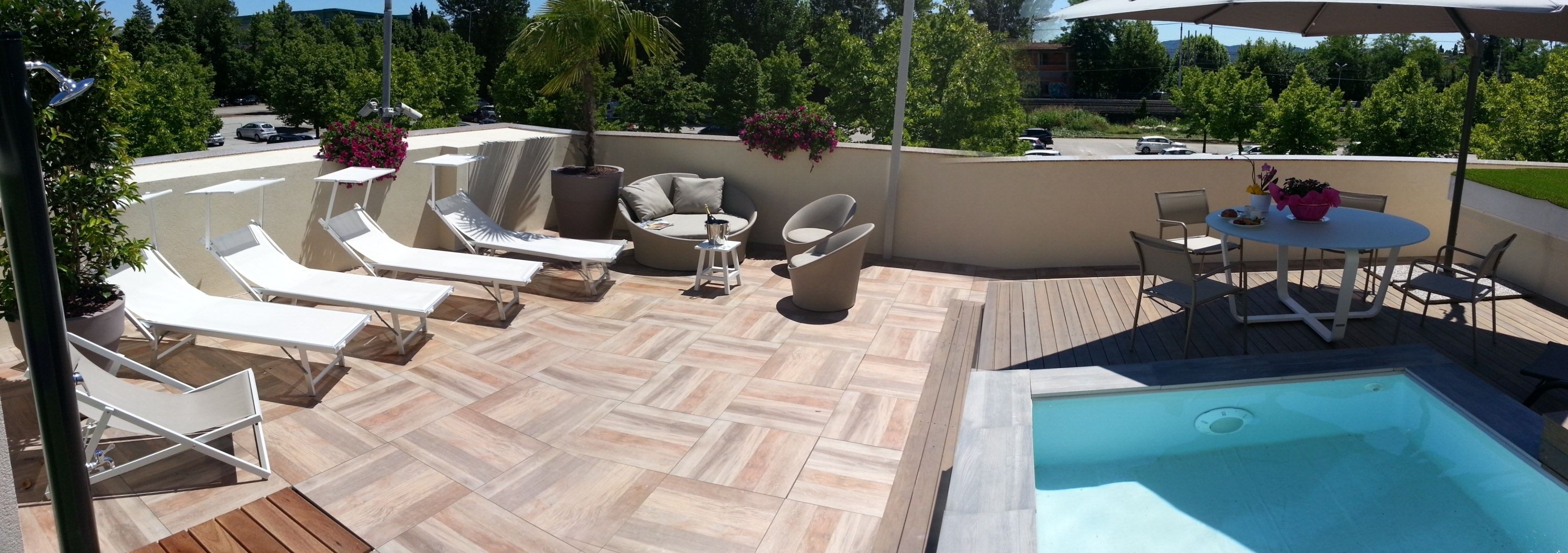 A rooftop patio with a swimming pool, lounge chairs, a table, and potted plants.
