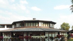 A modern building with a curved roof and a lion statue in front. - Hotel Novarello  (Granozzo con Monticello)