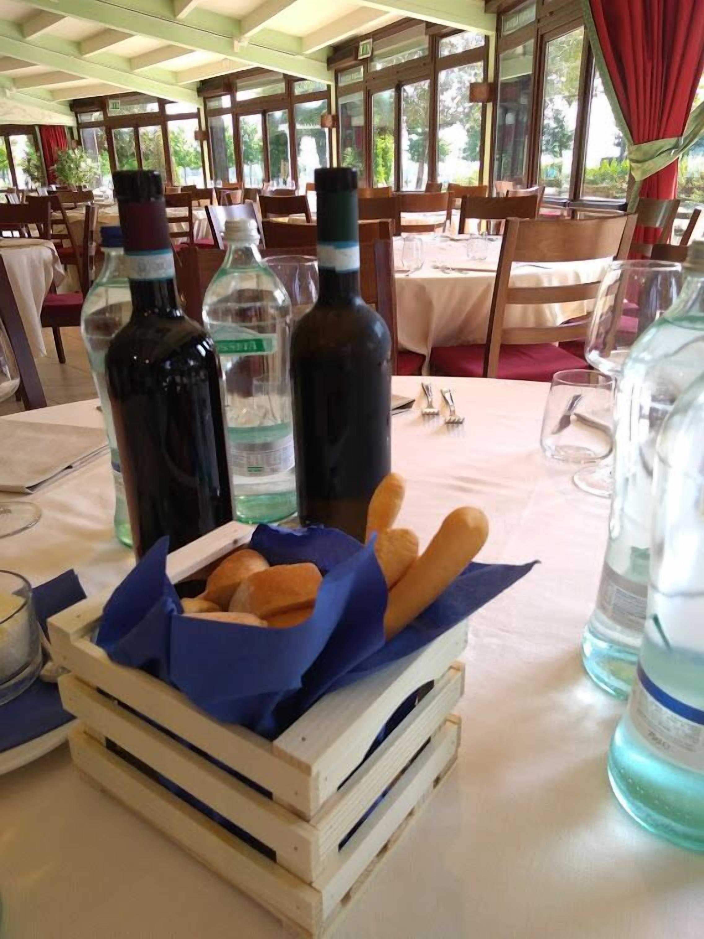 A dining area with tables set for meals, bottles of beverages, and a basket of bread.