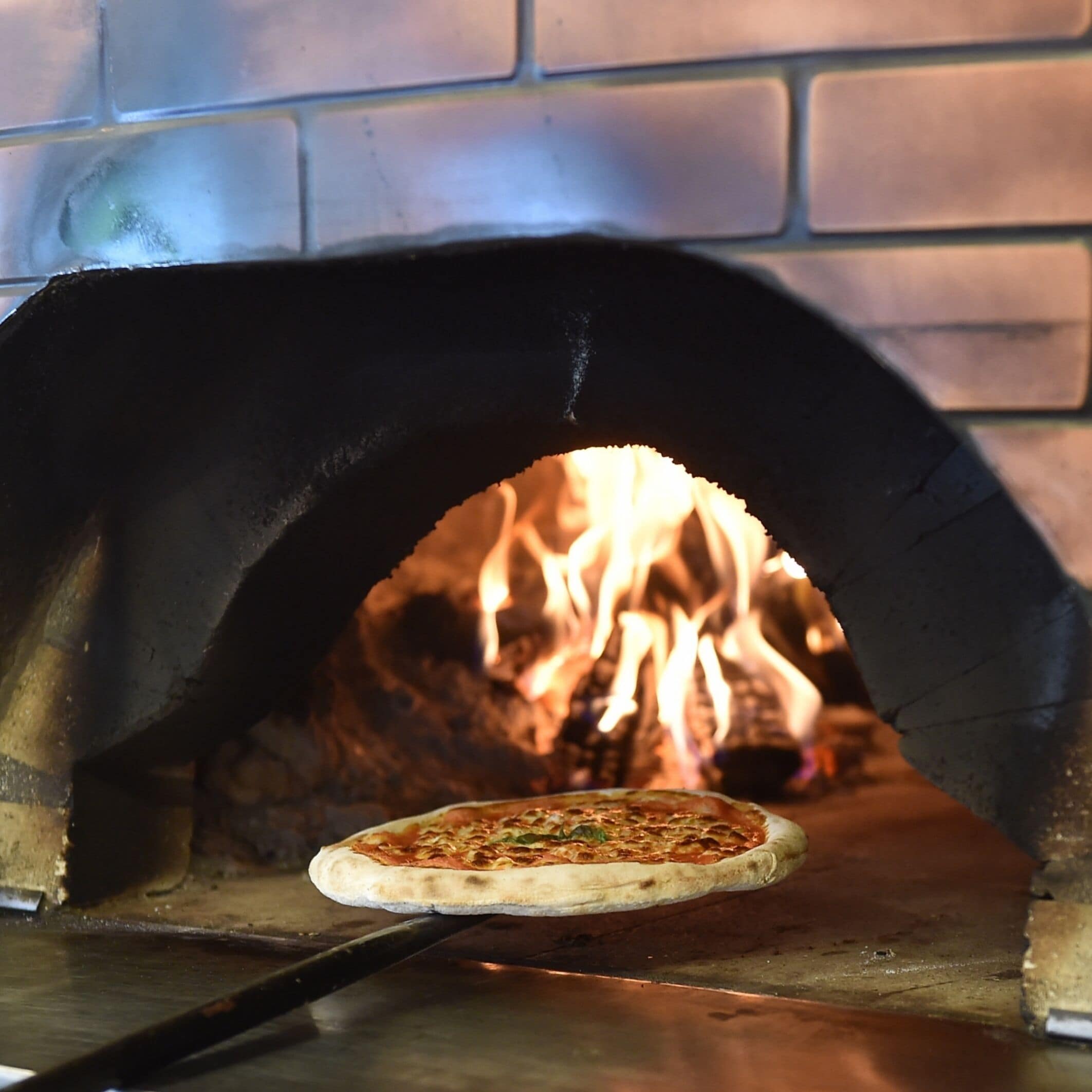 A pizza inside a brick oven with flames visible in the background.