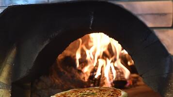 A pizza inside a brick oven with flames visible in the background.