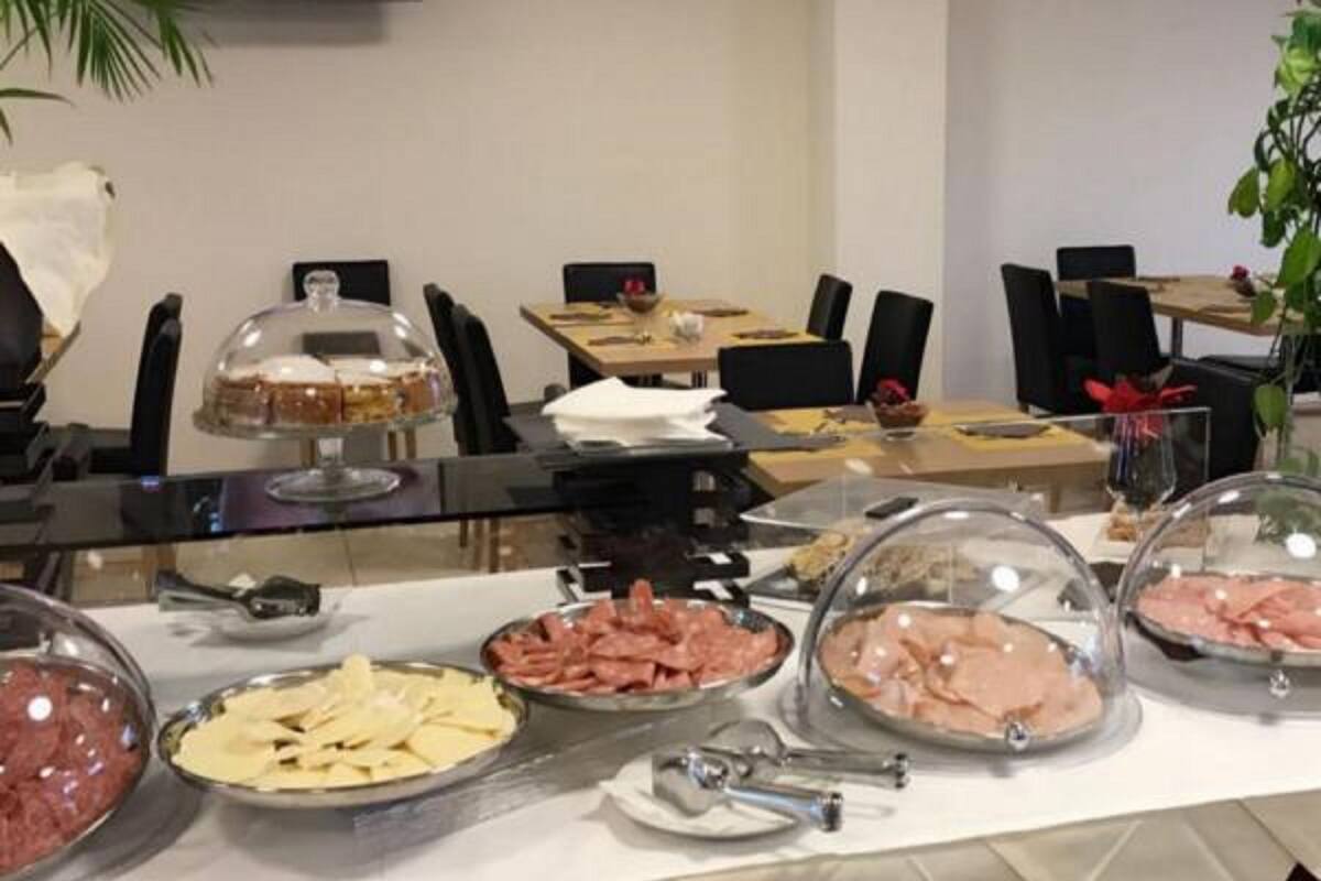 Montaje de bufé con diversas opciones de comida cubiertas por campanas de vidrio, incluyendo carnes y quesos, con platos y cubiertos sobre la mesa.