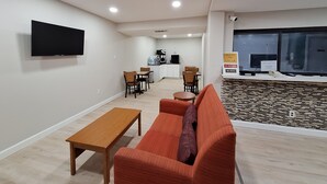 A modern living room with a sofa, a wooden table, and a TV mounted on the wall. - Budget Inn Roxboro (Roxboro)