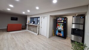 A spacious room with a wooden floor, a red sofa, a vending machine, a refrigerator, and a TV mounted on the wall. - Budget Inn Roxboro (Roxboro)