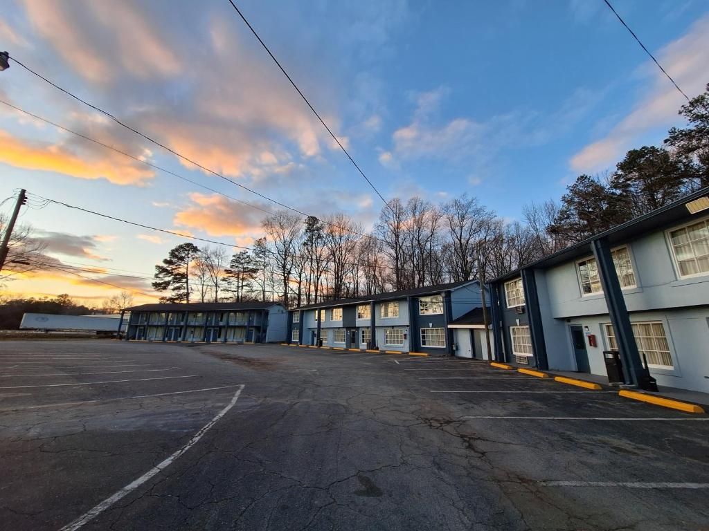 Un motel con varias habitaciones, un estacionamiento y una fila de árboles al fondo.