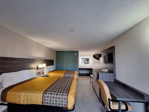 A hotel room with two beds, a desk, a chair, a mirror, and a window.
