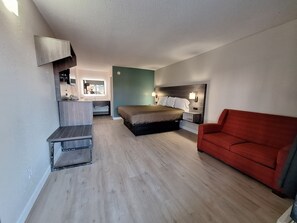 A compact bedroom with a bed, a red couch, a desk, and a mirror.