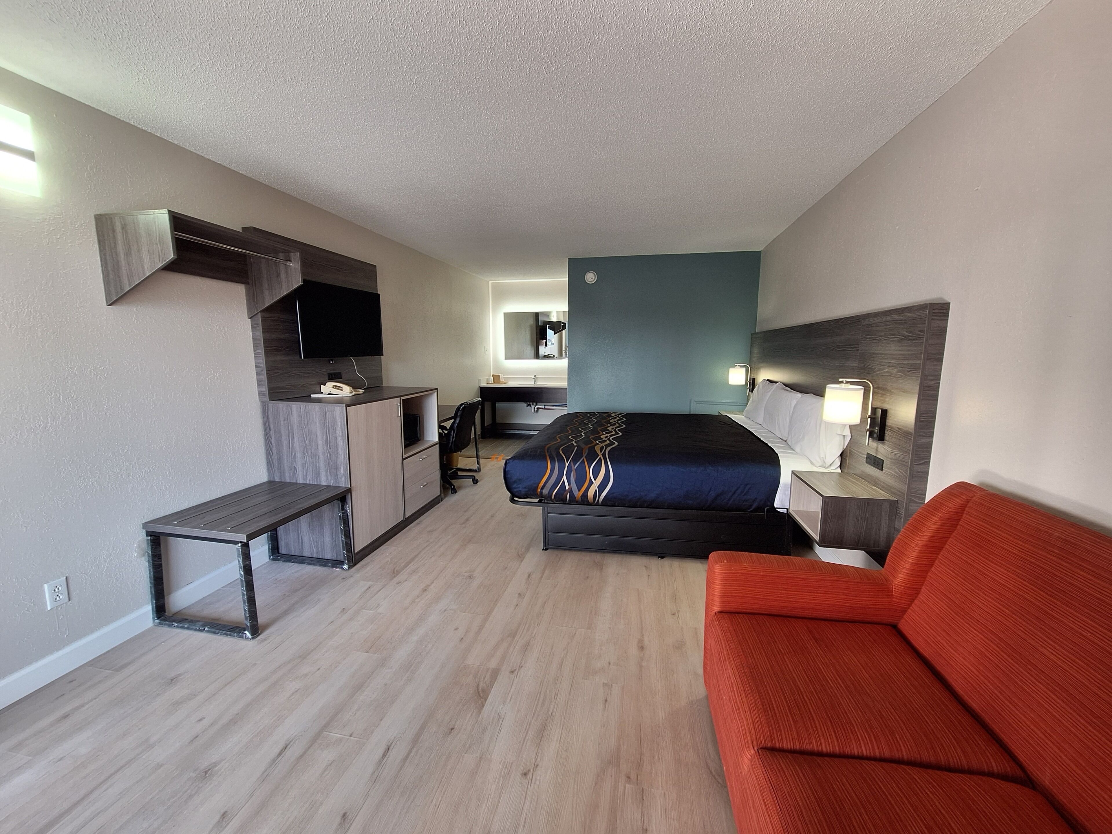 Una habitación de hotel moderna con cama, escritorio, silla, sofá y televisor.