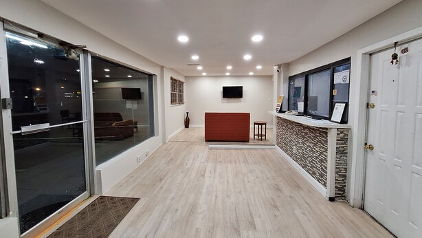 A hotel reception area with a wooden floor, a reception desk, a TV mounted on the wall, and a sliding glass door on the left. - Budget Inn Roxboro (Roxboro)