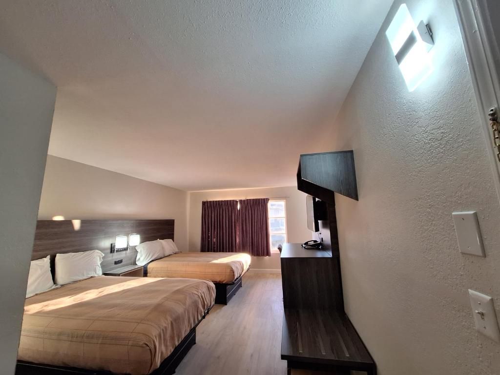 A hotel room with two beds, a flat-screen TV mounted on the wall, and a window with curtains.