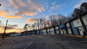 A motel with multiple rooms, a parking lot, and a view of trees and sky. - Budget Inn Roxboro (Roxboro)