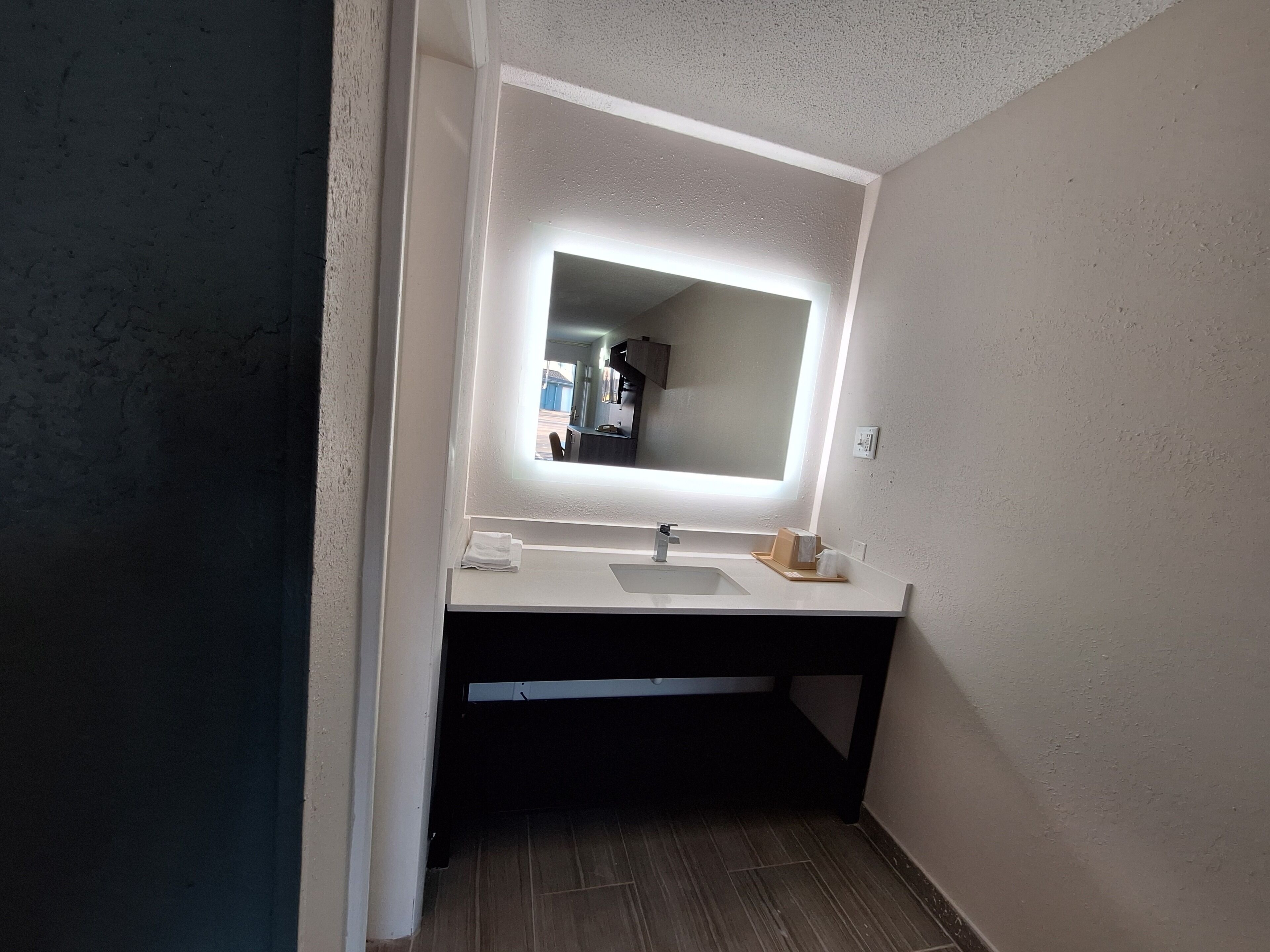 Un baño con un lavamanos blanco, un espejo y una lámpara sobre el espejo.