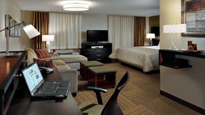 A hotel room with a bed, a desk with a laptop, a TV, and a bedside table. - Staybridge Suites Dearborn MI by IHG (Dearborn)