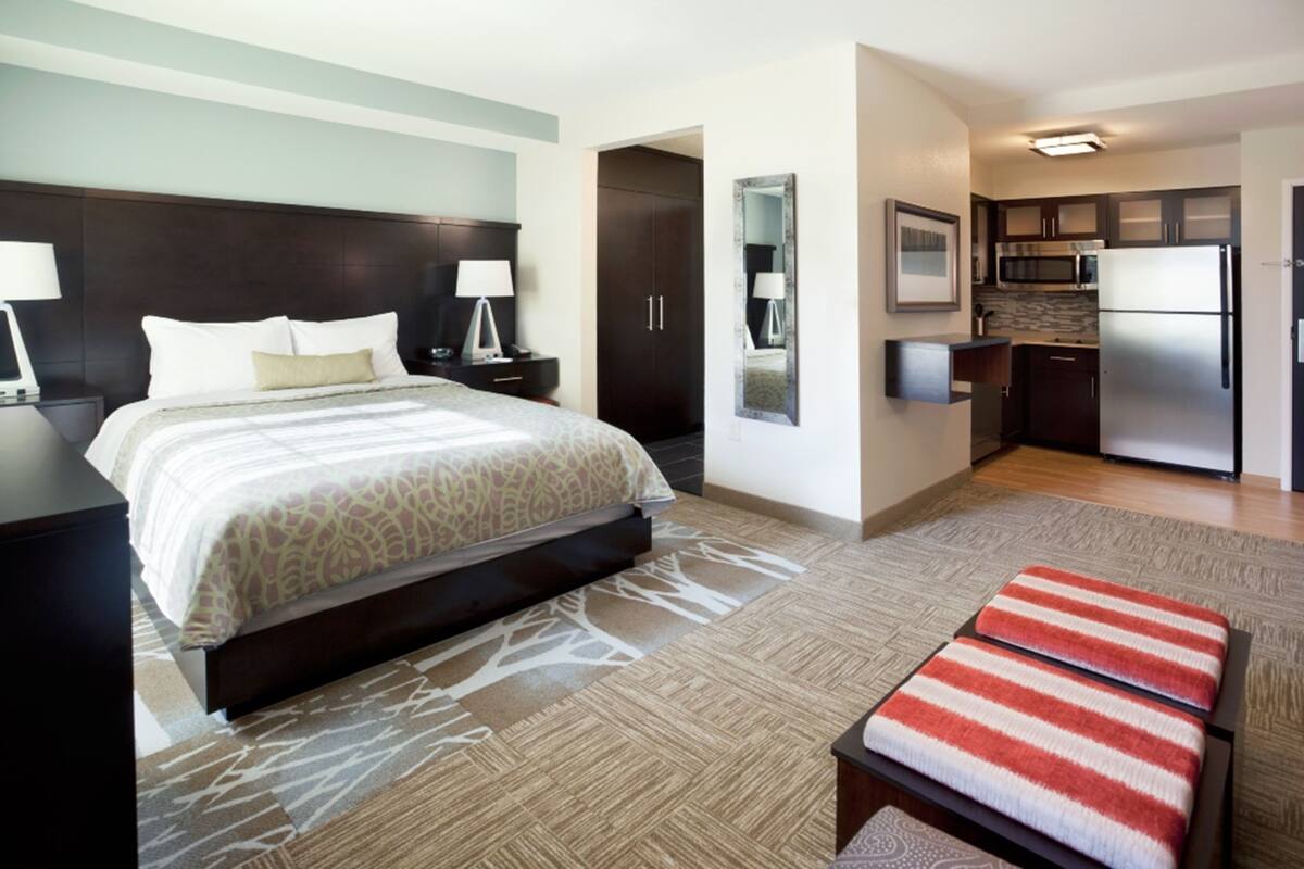 A hotel room with a bed, bedside tables, a mirror, a kitchenette, and a bathroom.