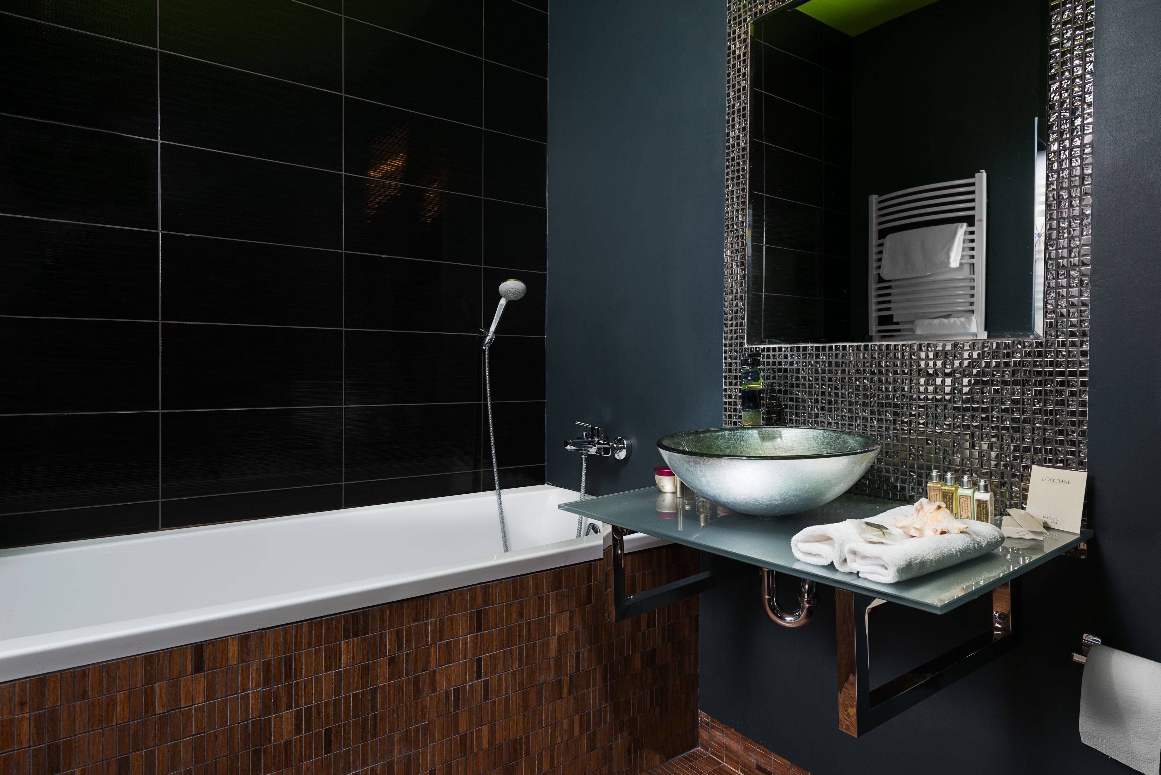 A modern bathroom with a glass vanity, a large bowl sink, and a black tiled shower area.