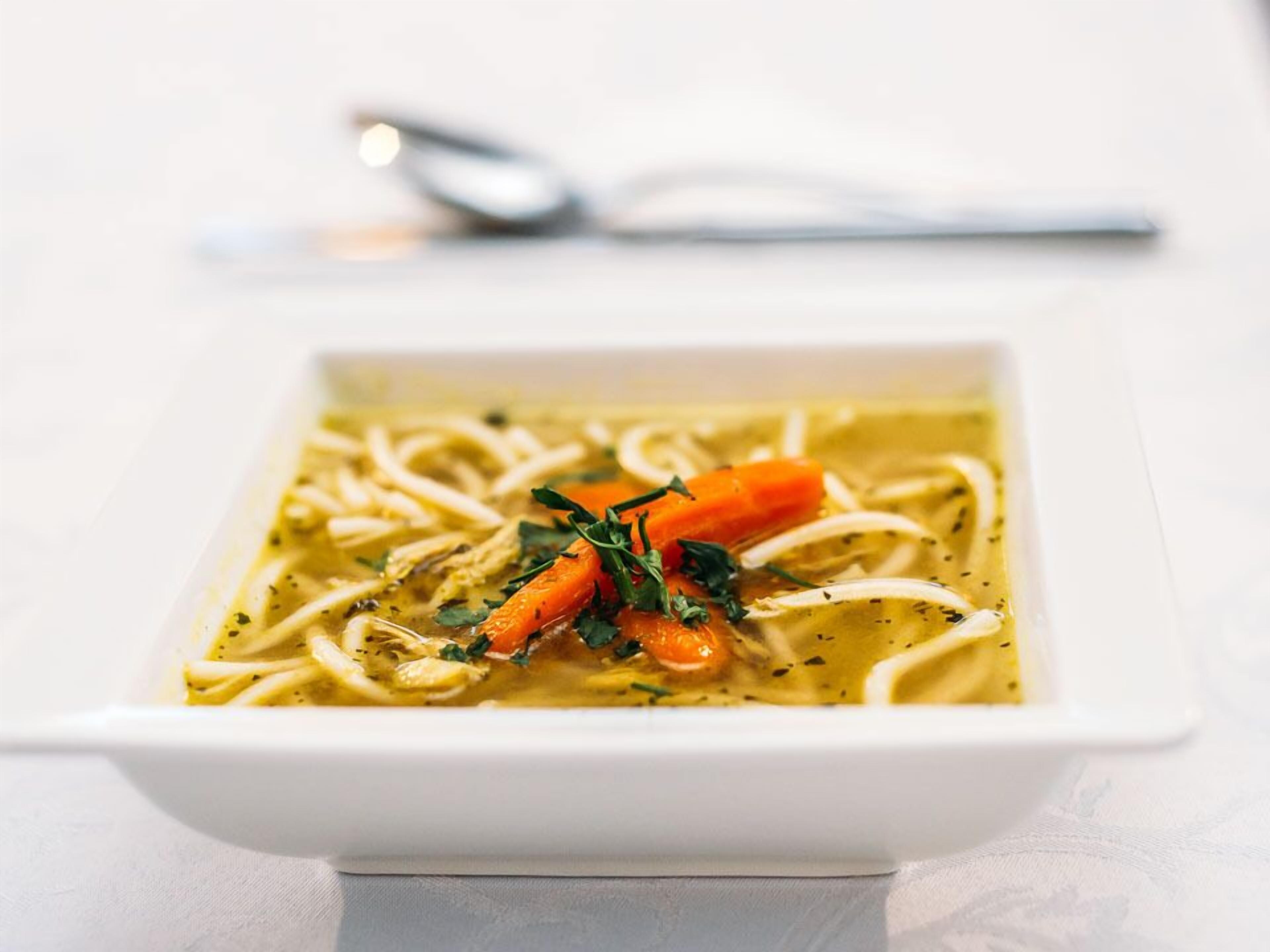 A bowl of soup with noodles, carrots, and herbs.