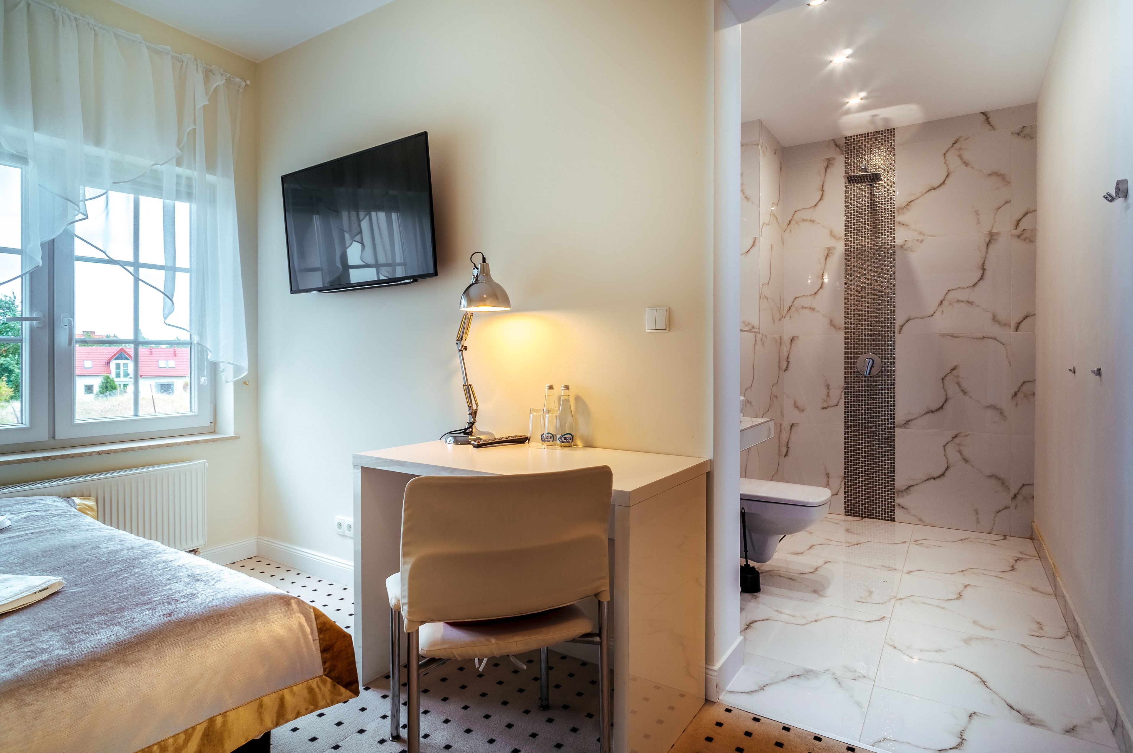 A bedroom with a bed, a desk with a chair, a TV, and a bathroom with a shower and toilet.