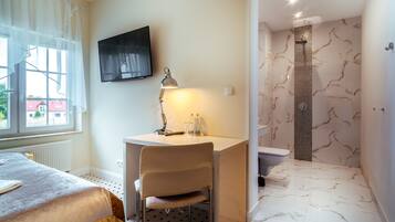 A bedroom with a bed, a desk with a chair, a TV, and a bathroom with a shower and toilet.