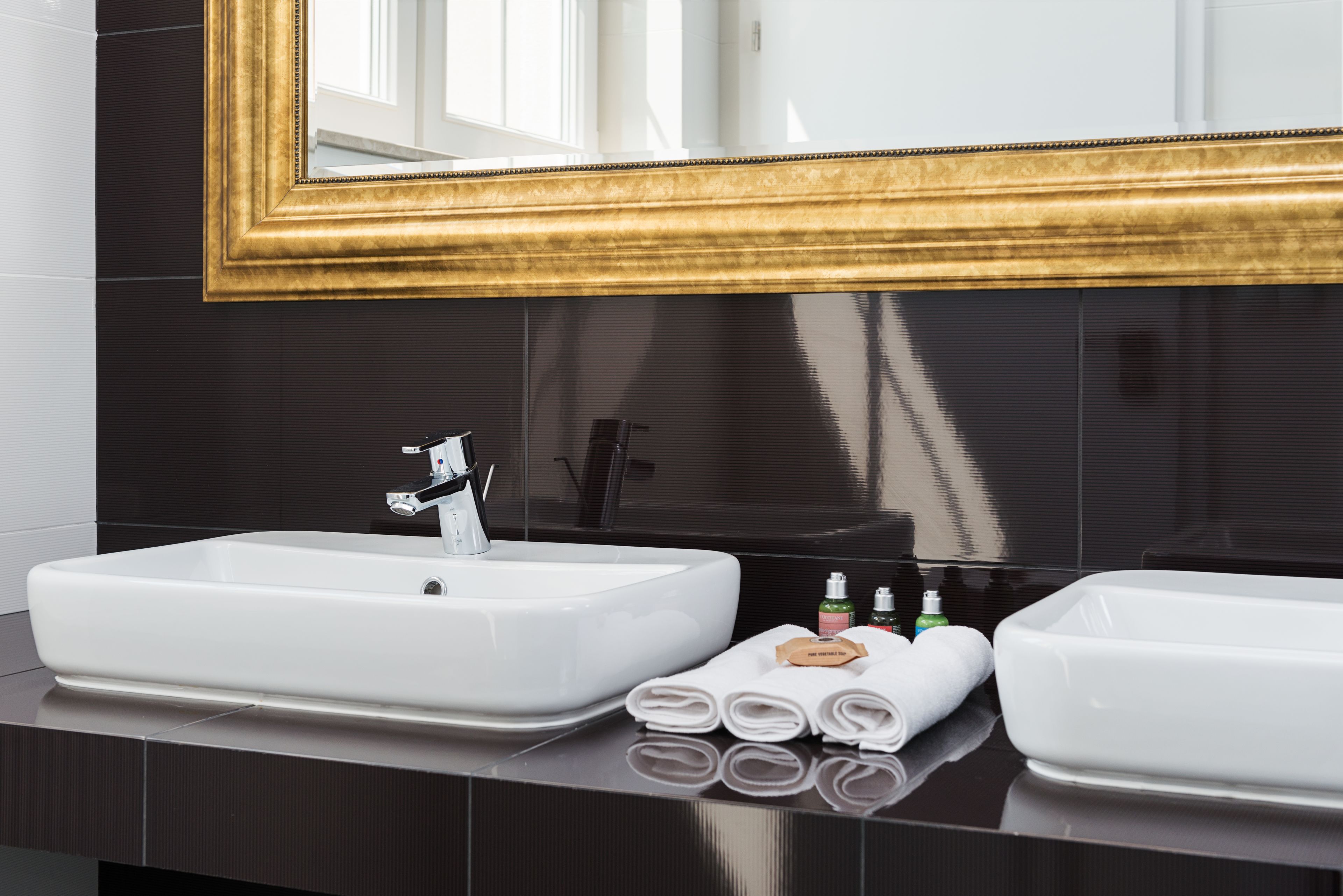 Een badkamer met twee witte wasbakken, een spiegel met gouden lijst en toiletartikelen op het aanrecht.