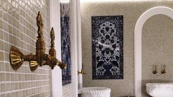 Un baño con un lavamanos grande y ornamentado, un grifo de bronce empotrado en la pared y un salpicadero decorado con azulejos.