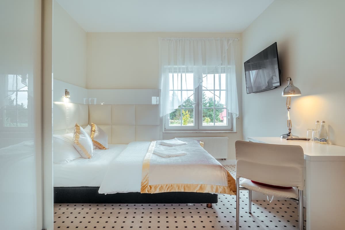 A hotel room with a bed, a desk, a chair, a TV, and a window with curtains.