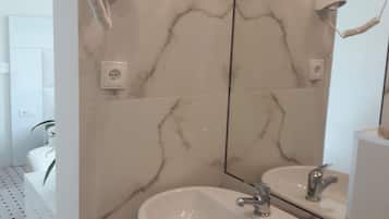 Un baño con pared de mármol, un lavamanos, un espejo y un secador de pelo fijado a la pared.