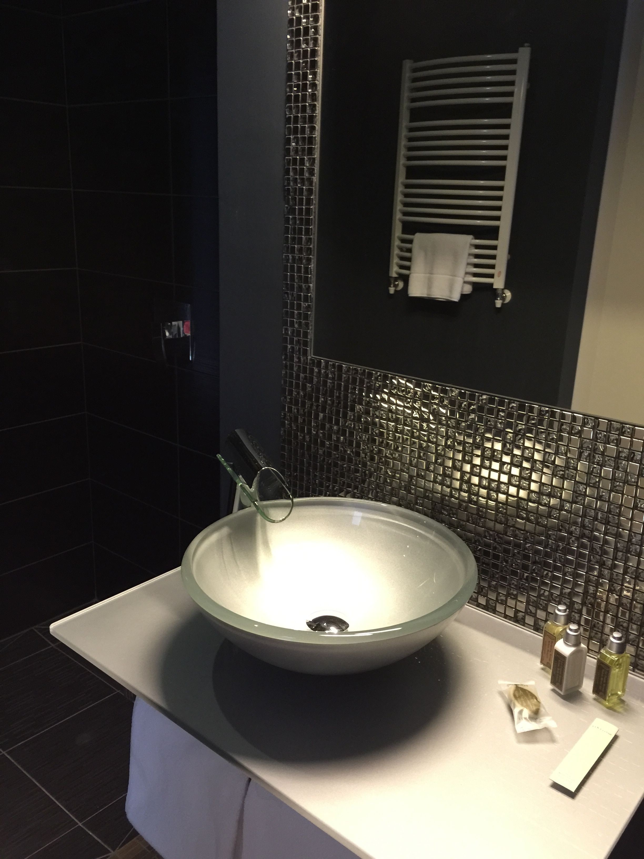 A modern bathroom with a large glass sink, a towel rack, and a mirror.