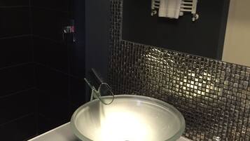 A modern bathroom with a large glass sink, a towel rack, and a mirror.