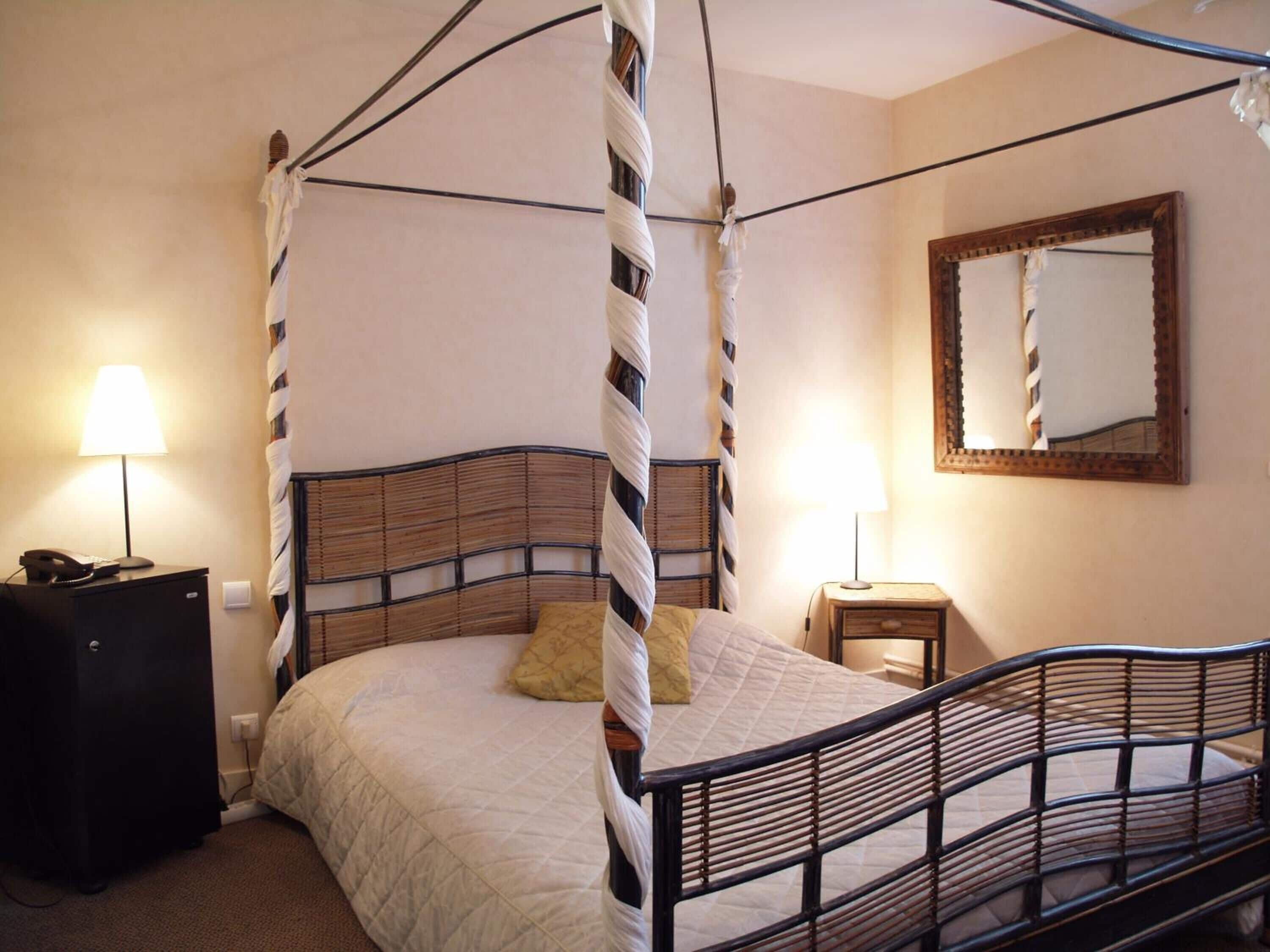 Un lit à baldaquin à quatre poteaux, avec une tête de lit en bois, des tables de chevet avec des lampes et un miroir au mur.
