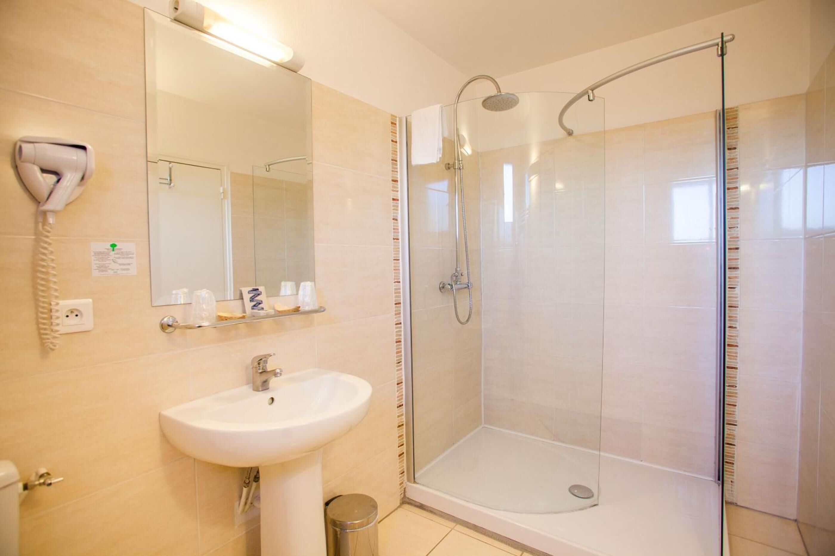 Un baño moderno con ducha de vidrio, lavamanos blanco y un secador de pelo fijado en la pared.