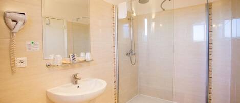 Un baño moderno con ducha de vidrio, lavamanos blanco y un secador de pelo fijado en la pared.