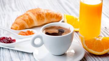 A breakfast setting with a croissant, a cup of coffee, a glass of orange juice, and a plate with jam and a spoon.