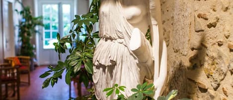 A statue in a hallway with stone walls and potted plants.