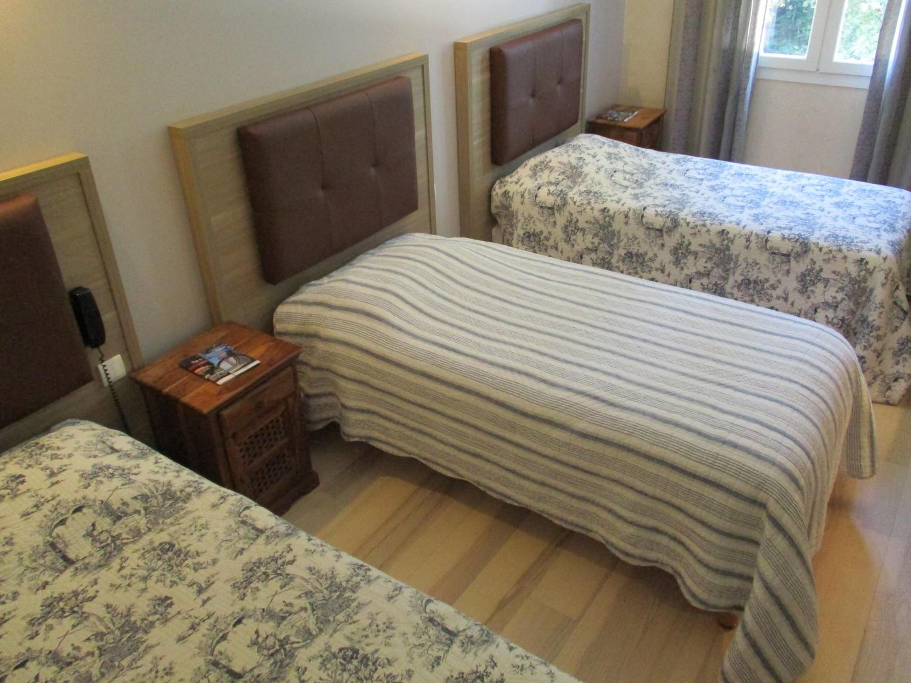 Een hotelkamer met twee bedden, elk met een hoofdbord en een bedspreidek met bloemenprint. Er staat een houten nachtkastje met een telefoon en een tijdschrift.