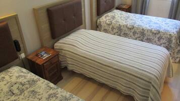 Een hotelkamer met twee bedden, elk met een hoofdbord en een bedspreidek met bloemenprint. Er staat een houten nachtkastje met een telefoon en een tijdschrift.
