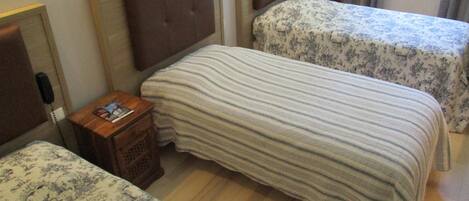 A hotel room with two beds, each with a headboard and a floral-patterned bedspread. There is a wooden nightstand with a telephone and a magazine.