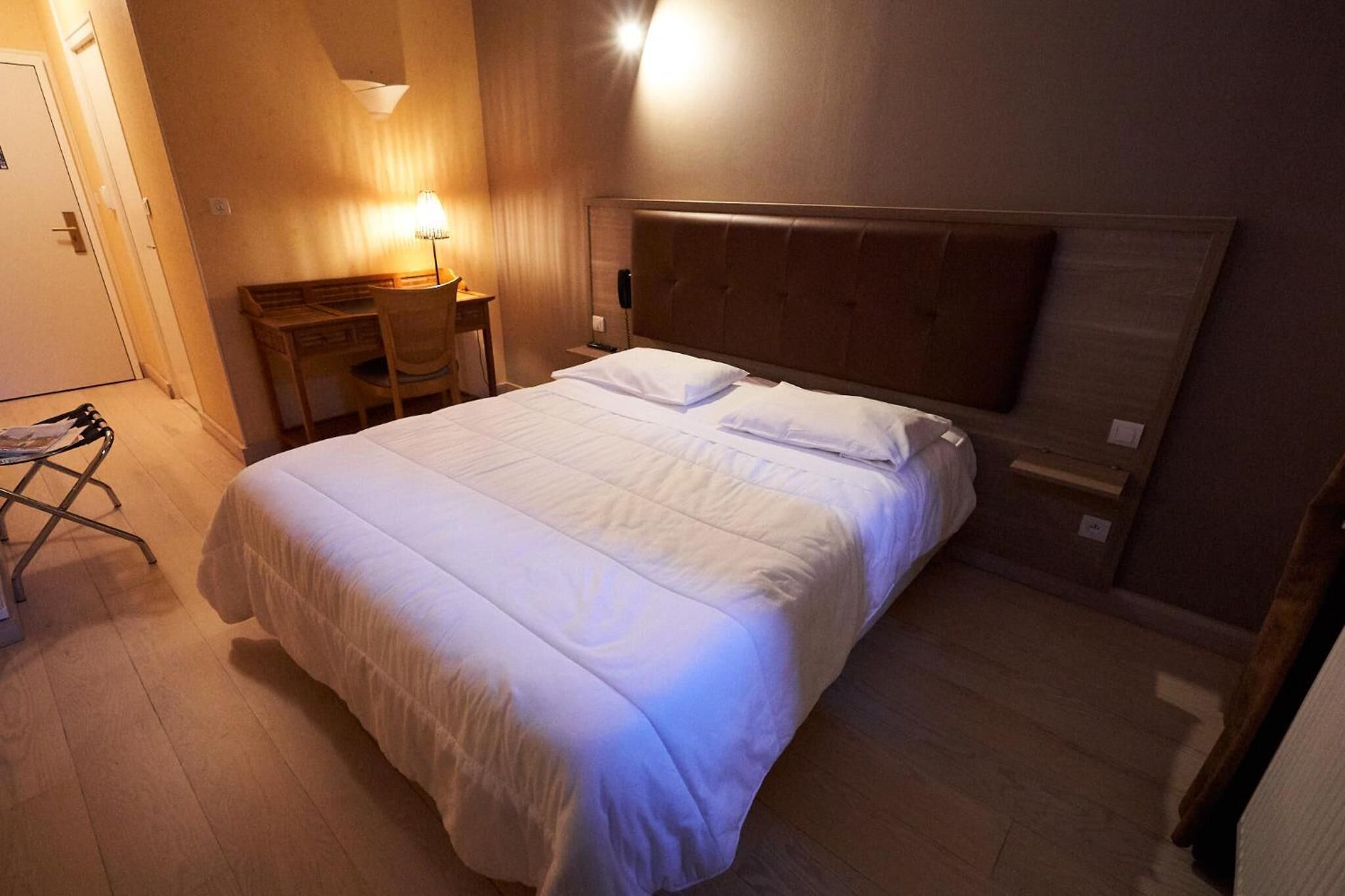 A neatly made bed with white linens in a hotel room.
