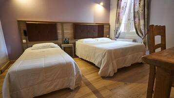 Habitación de hotel con dos camas individuales, cabecera de madera, mesita de noche con lámpara y ventana con cortinas.