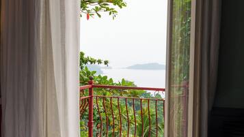 Un dormitorio con cama, ventana y vista a un balcón con vegetación y un cuerpo de agua.