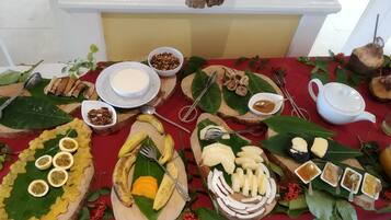 A table with various food items and utensils, including bananas, mango slices, and bowls of nuts and sauces.