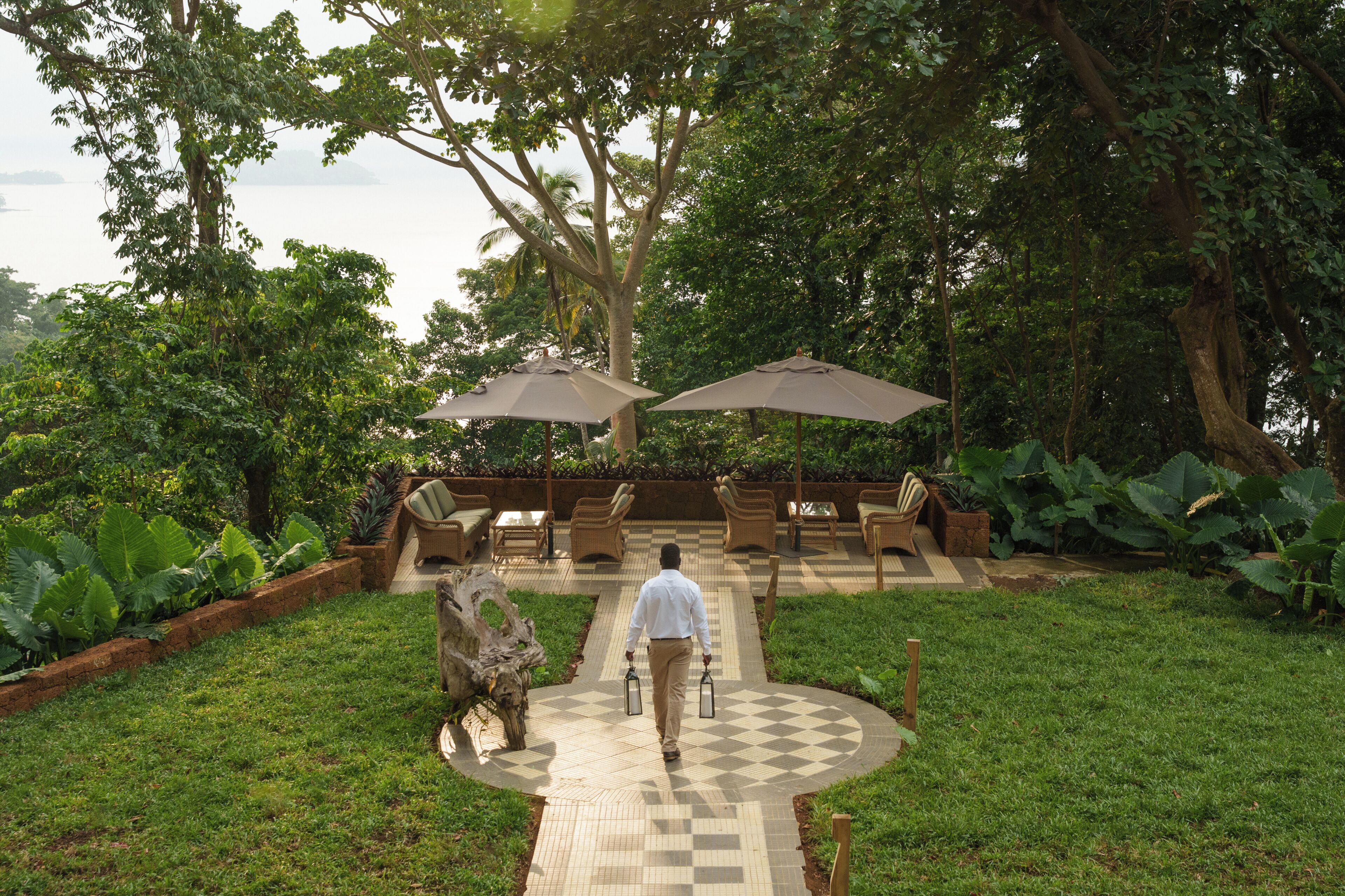 A garden patio with outdoor furniture and umbrellas, surrounded by lush greenery.