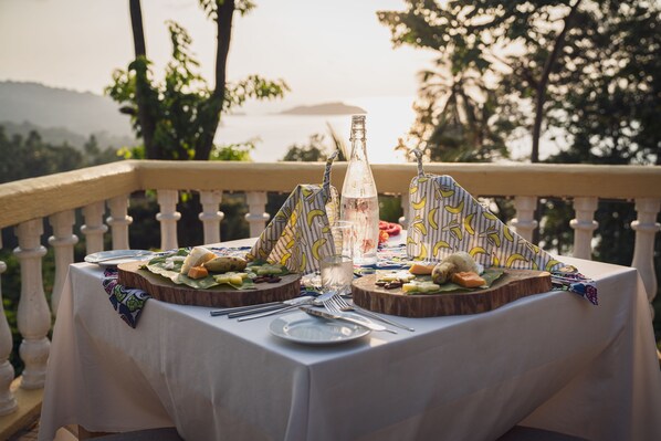 A table set for a meal with a bottle and glasses, surrounded by a balustrade and greenery.
